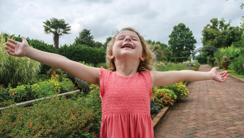 A happy girl with her arms spread wide in the garden